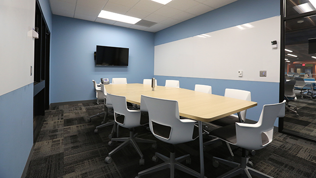 A meeting room featuring a large table with 10 chairs around it, with a TV on the wall.