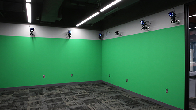 A room with cameras around the top of the wall and the wall painted chroma key green.
