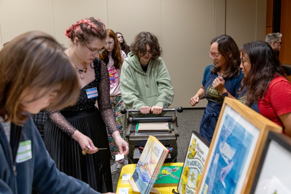Teenagers looking at prints and using a printing press