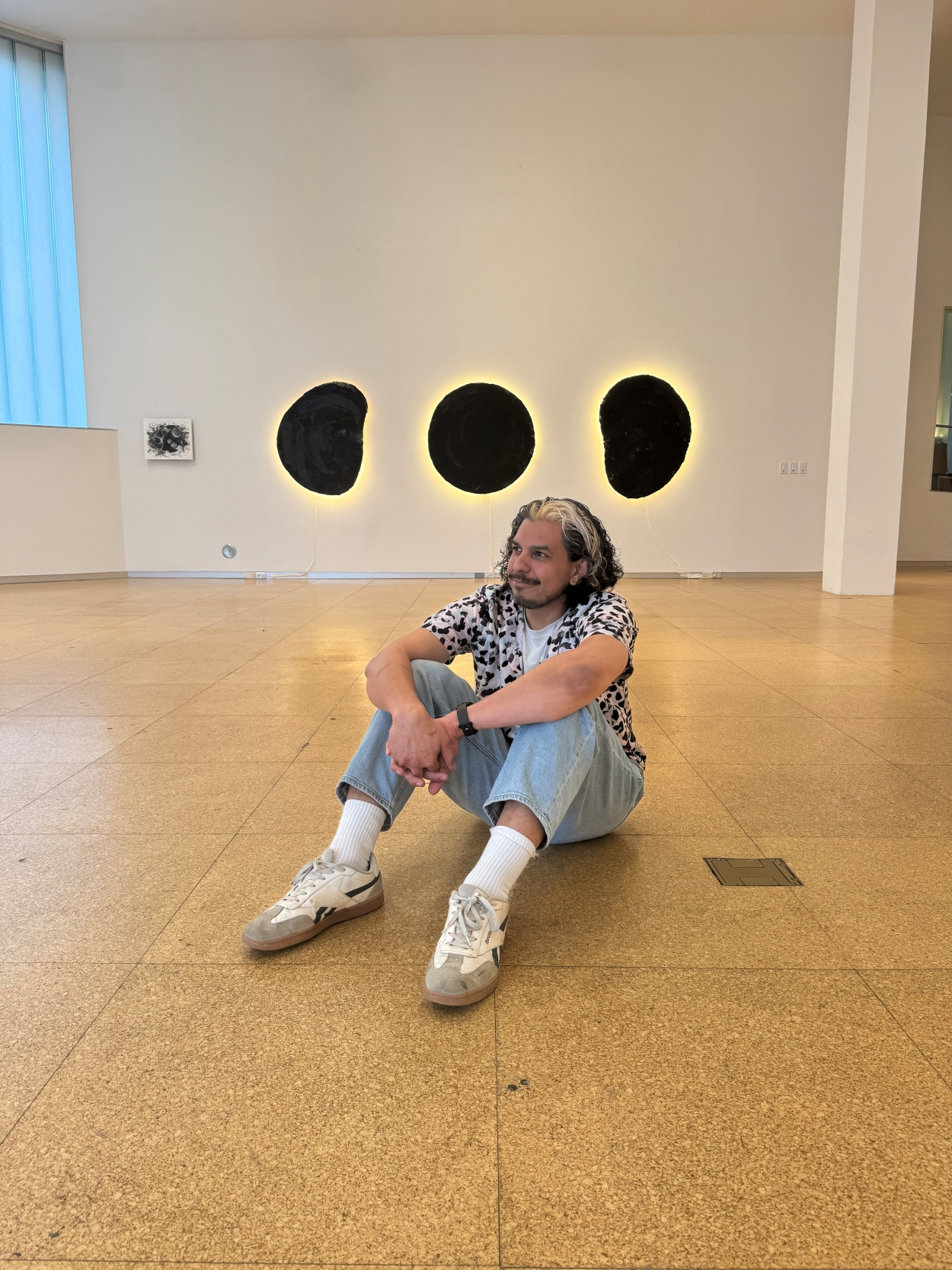 Man sitting down on a wooden floor in front of a white wall